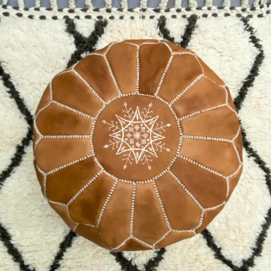 Pouf marocain en cuir miel posé sur tapis berbère Beni Ouarain – décoration artisanale marocaine