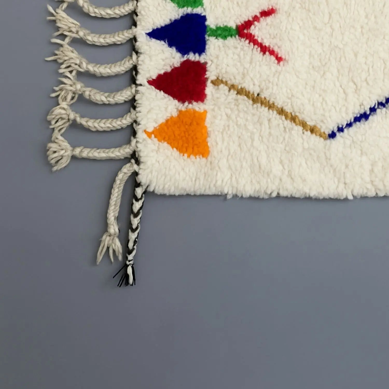 Détail d’un tapis berbère Azilal avec motifs géométriques colorés sur fond gris.