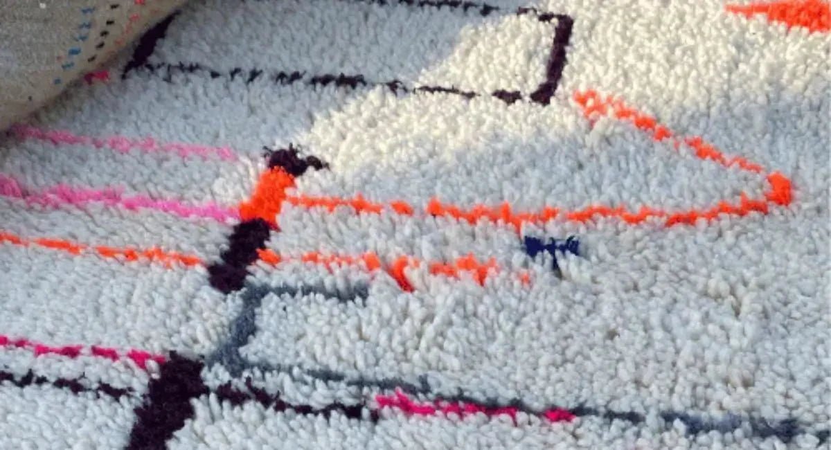 gros plan sur un tapis berbère moderne en laine blanche avec motifs géométriques orange, rose et noir – fait main au Maroc.