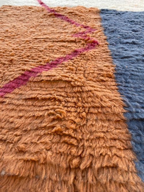 Gros plan sur la laine terracotta du tapis Beni Ouarain Anzar, avec motif géométrique rose et contraste bleu.