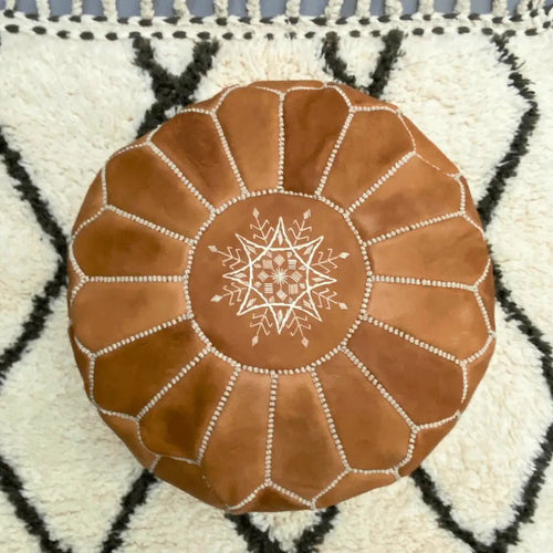 Pouf marocain en cuir miel posé sur tapis berbère Beni Ouarain – décoration artisanale marocaine