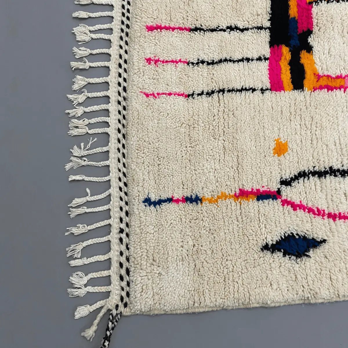Détail du tissage en laine naturelle du tapis Azilal – couleurs vives rose, orange et bleu sur fond crème